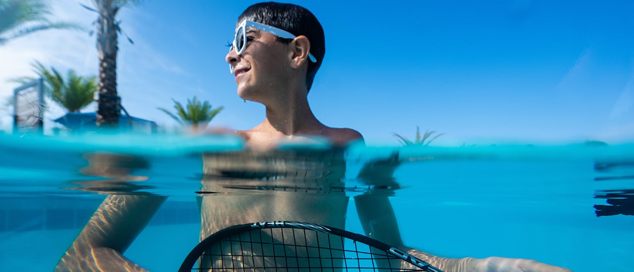 boy in pool with goggles playing air guitar on a tennis racket in wylder