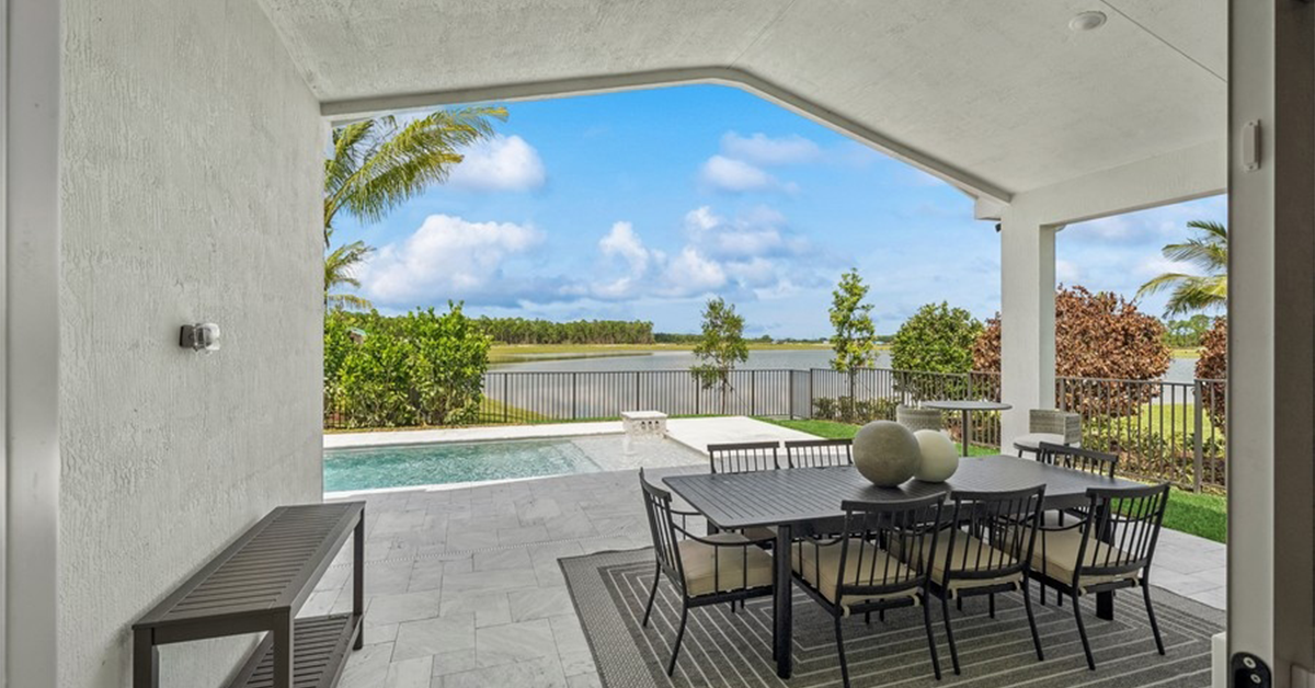Covered lanai with dining table overlooks pool and water view.