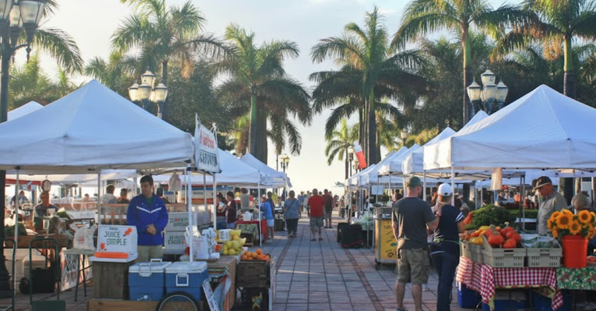 Open-air farmers market with white tents and palm trees.
