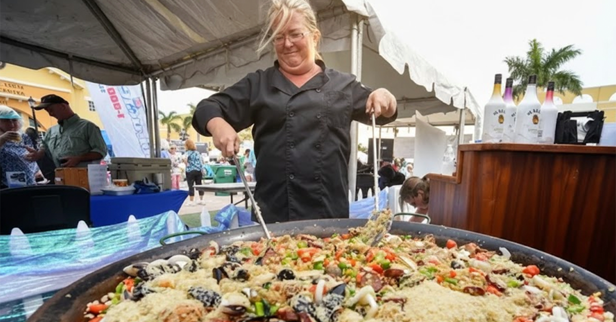 Chef cooking large seafood paella at outdoor festival.