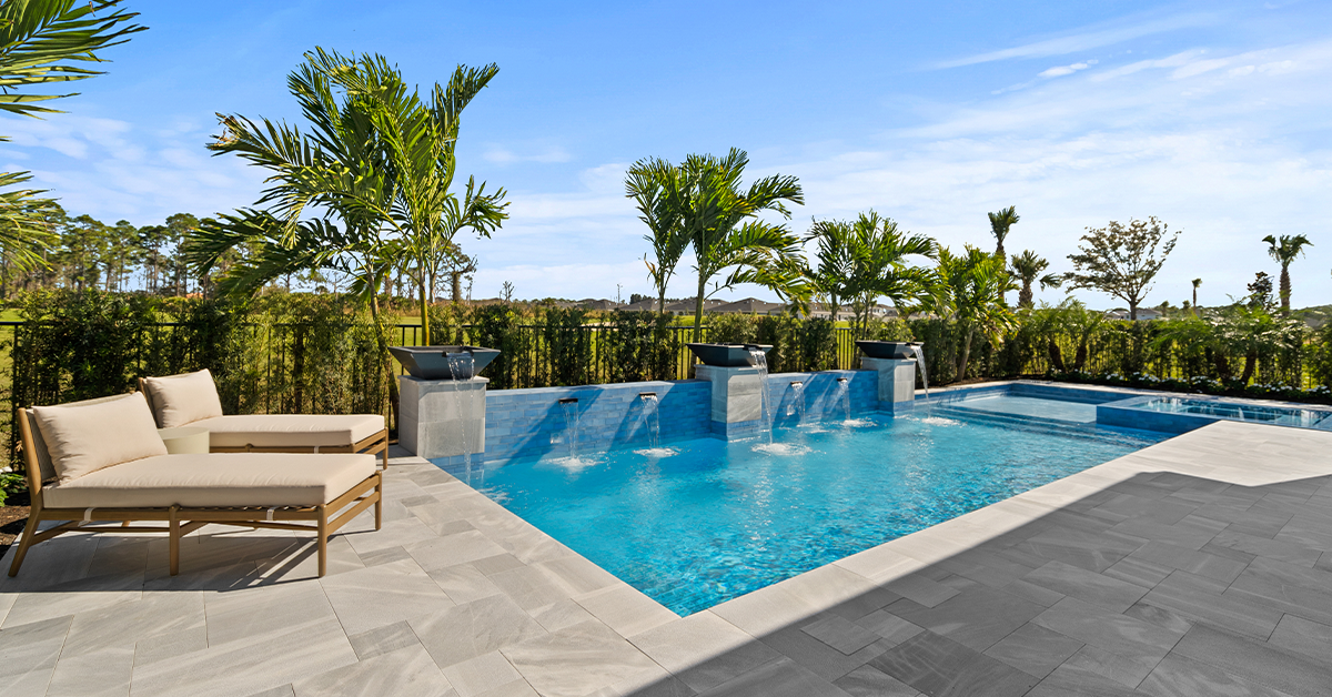 Backyard pool with water features, palm trees, and patio lounge chairs