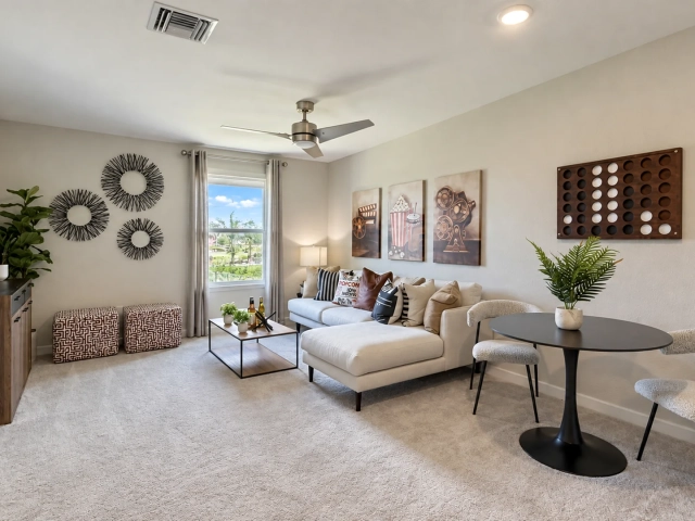 Carpeted media room with a cream sectional sofa, a round black table with chairs, and movie-themed wall art.