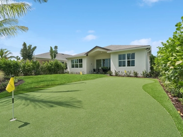 Backyard putting green with two flagged holes behind a white stucco home with a covered patio and outdoor dining table.