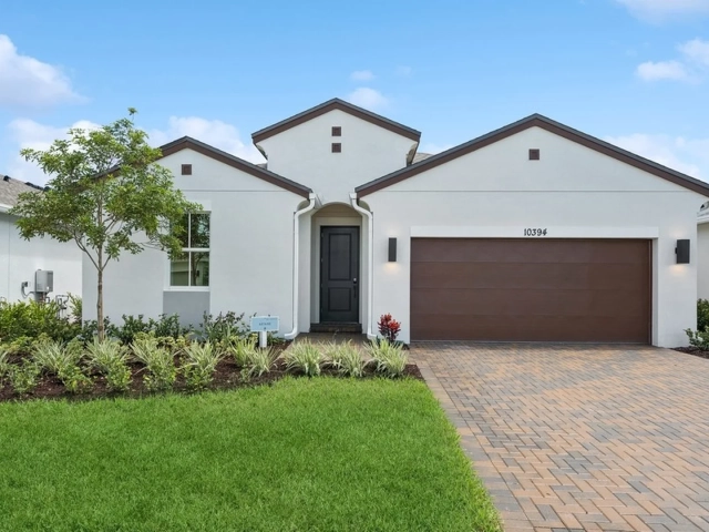 Single-story white stucco model home with a dark wood garage door, arched entry, and paver driveway, address 10394.