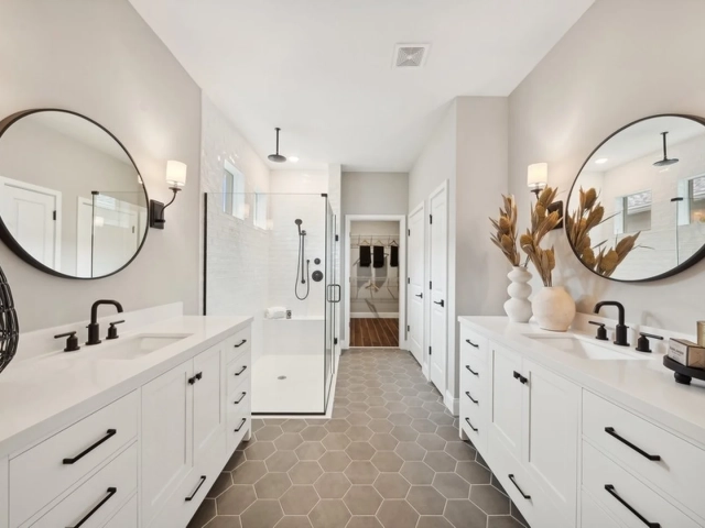 Bathroom with two white vanities, round black-framed mirrors, and a glass walk-in shower with hexagon tile flooring.