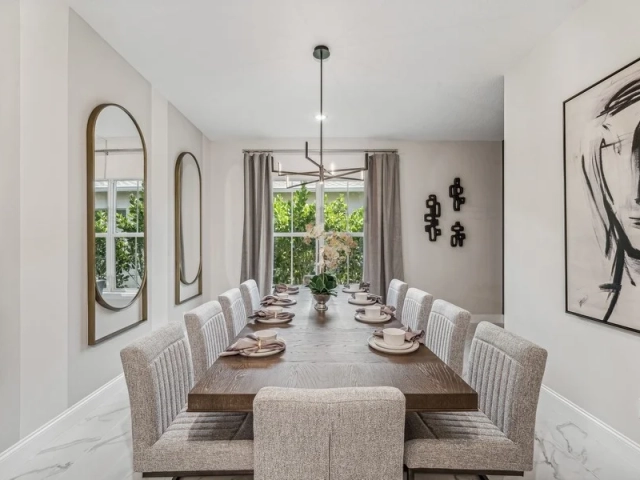 Dining room with a long wood table set for ten guests, gray upholstered chairs, and oval gold-framed mirrors on the wall.