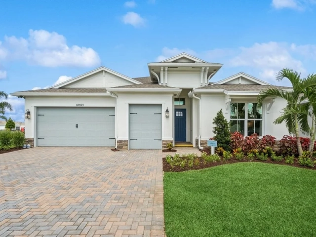 Single-story white stucco model home with two light gray garage doors, stone accents, and a paver driveway, address 10353.
