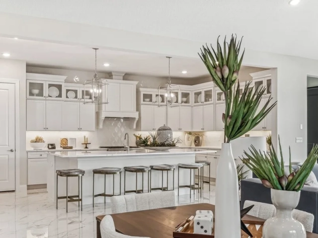 Kitchen island with five barstools and pendant lighting, opening into a living room with a dark sectional sofa.