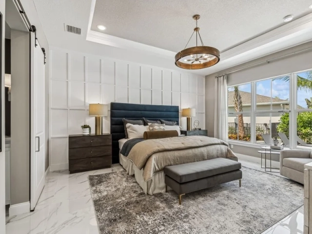 Primary bedroom with a navy upholstered bed, a paneled white accent wall, a gray bench at the foot of the bed, and a large window with a golf course view.