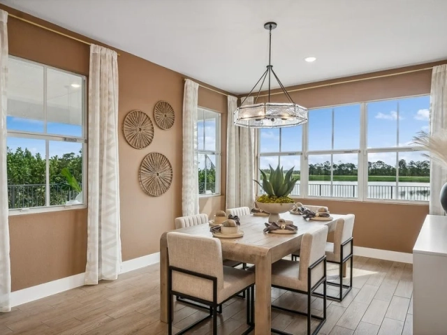 Dining room with a wood table set for six, upholstered chairs, and large windows overlooking a lake.