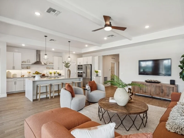 Open living room with terracotta sectional sofas, a wall-mounted TV, and an open white kitchen with an island in the background.