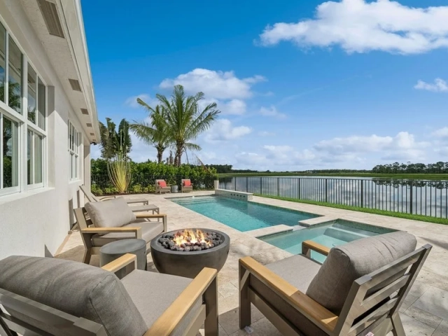 Covered patio with lounge chairs around a fire pit, a pool and spa, and a screened lake view in the background.