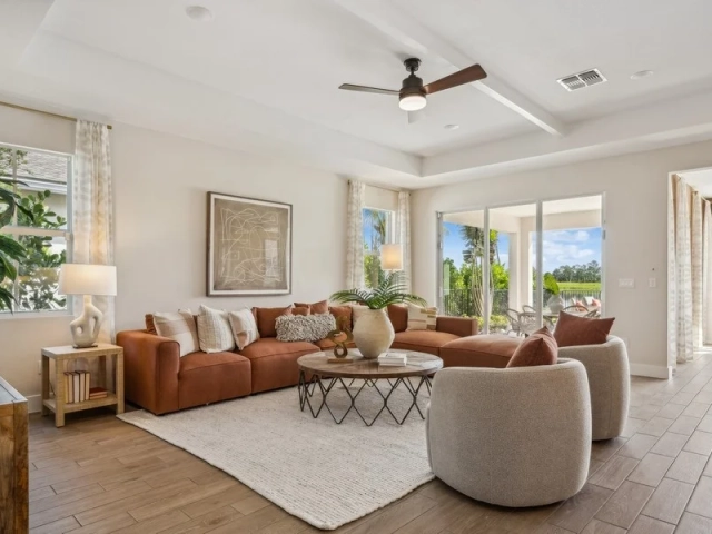 Living room with a cognac leather sectional sofa, two gray swivel chairs, and sliding glass doors overlooking a lake.
