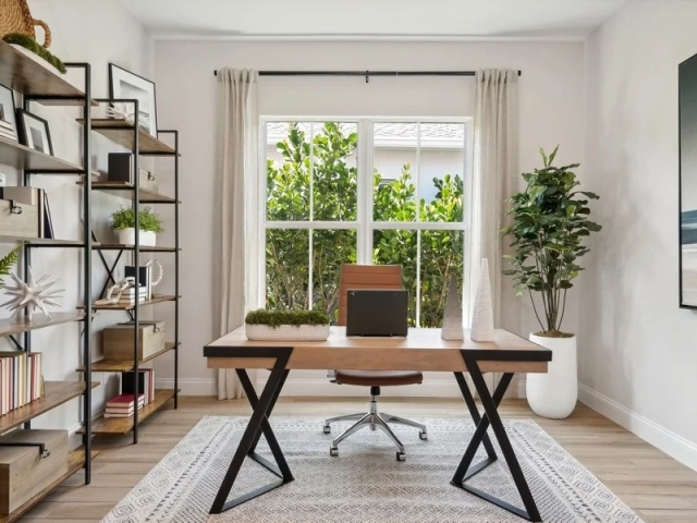 Home office with a wood desk, brown leather office chair, and a tall black metal bookshelf with books and decor.