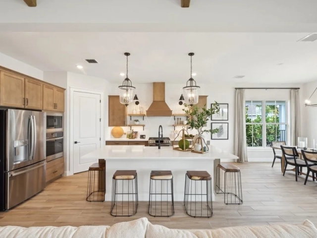 Kitchen island with four wire-frame barstools and glass pendant lights, opening into a dining room with a chandelier.