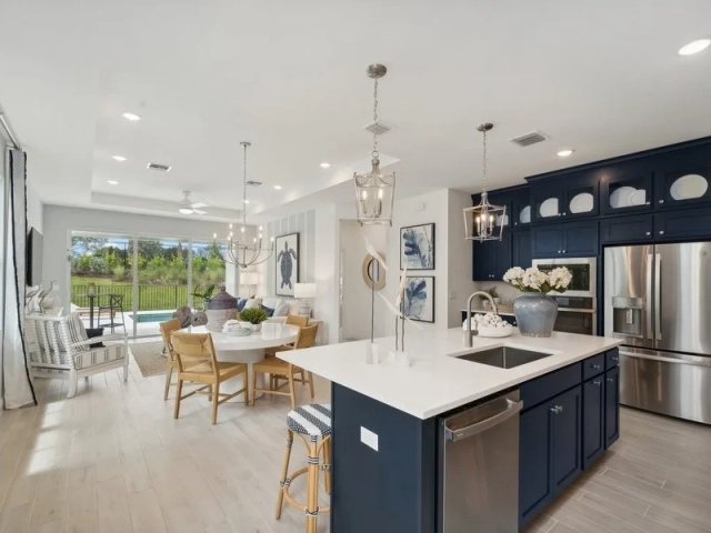Navy blue kitchen island with lantern pendants, opening into a dining area with a round table and a view of the pool through sliding glass doors.