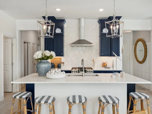 Kitchen with navy blue cabinets, an arabesque tile backsplash, a stainless steel range hood, and an island with striped barstools.