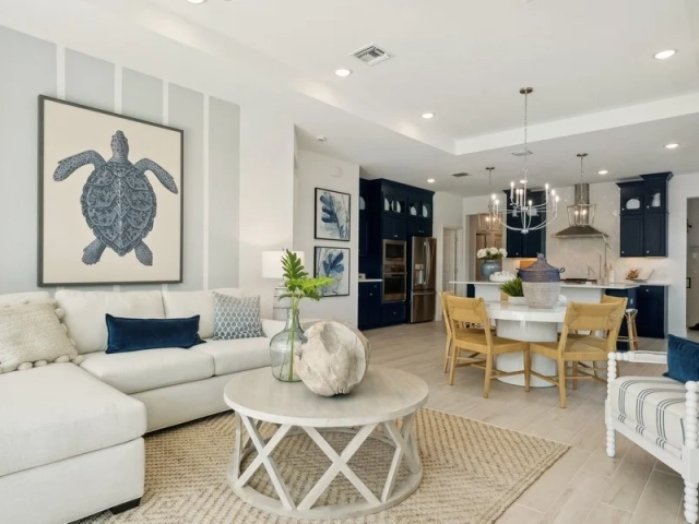Living room with a cream sectional sofa, a large sea turtle wall art print, and an open dining area and kitchen visible beyond.