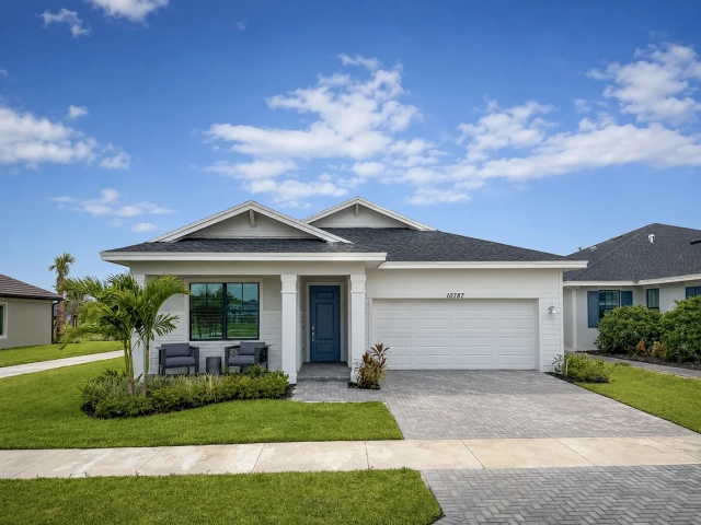 Single-story white model home with a navy front door, two dark outdoor chairs on the porch, and a two-car garage, address 10787.