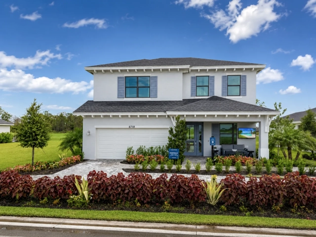 Two-story white model home with blue-gray shutters, a covered front porch with outdoor seating, and a two-car garage, address 6719.