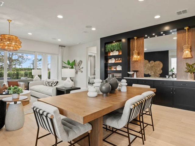 Dining room with a wood table, black-and-white striped chairs, woven pendant lights, and a dark built-in bar wall with open shelving.