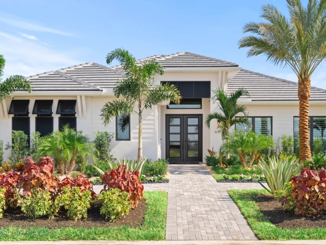 Single-story white model home with black shutters, a tiled roof, dark double front doors, and red-leafed landscaping, address 6703.