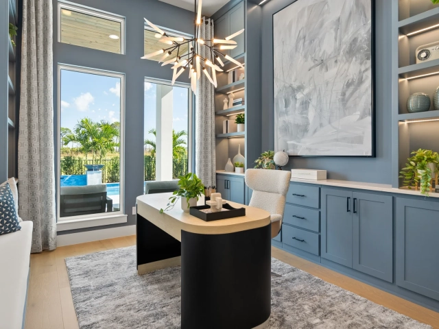 Home office with blue built-in shelving, a black and wood desk, a branch-style chandelier, and a window overlooking a pool.