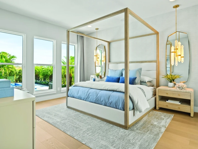 Primary bedroom with a light wood canopy bed, blue and white bedding, and gold oval mirrors with pendant lights on either side.