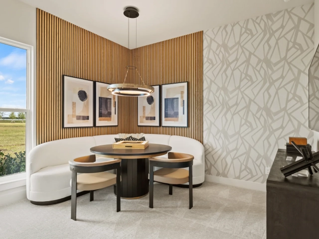 Curved white banquette seating around a round dark wood table, with a wood slat accent wall and framed abstract art.