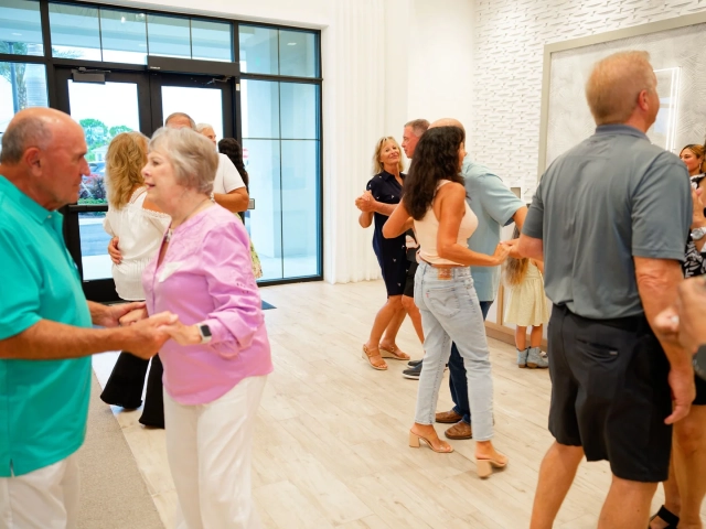 Multiple couples dancing hand-in-hand in a bright, glass-walled lobby with light wood flooring.
