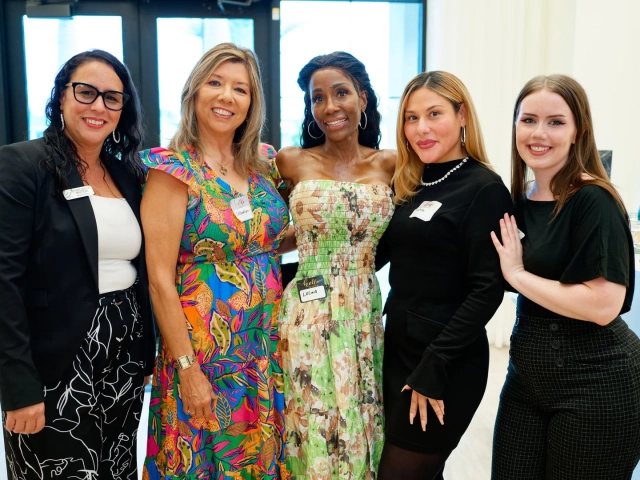 Five women posing together indoors at night near glass entrance doors, one wearing a name tag reading Lelisa.