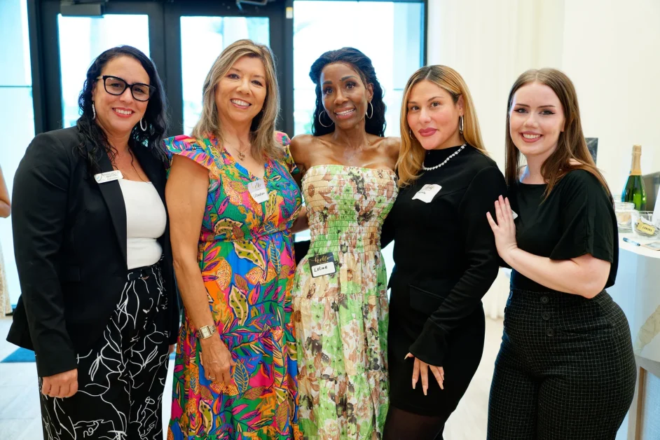 Five women posing together indoors at night near glass entrance doors, one wearing a name tag reading Lelisa.