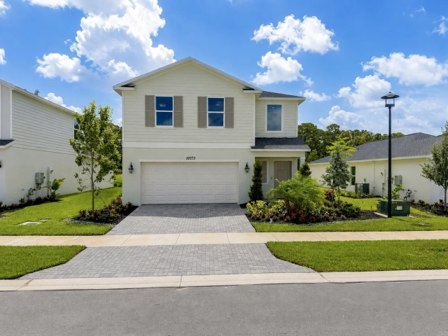 Two-story home with pale yellow siding, taupe window shutters, a two-car garage, and a paver driveway.