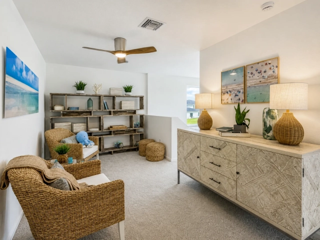 Carpeted loft with two woven wicker armchairs, a wood bookshelf, and a wood-topped console table with beach-themed art.